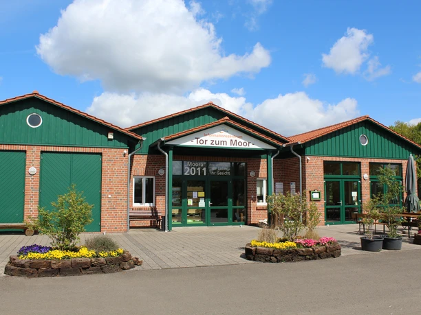 The "Tor zum Moor" visitor center with its red brick building and green doors under a blue sky.