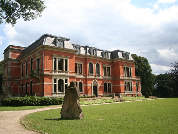Historic red-brick Etelsen Castle with decorative façade set in a green park.