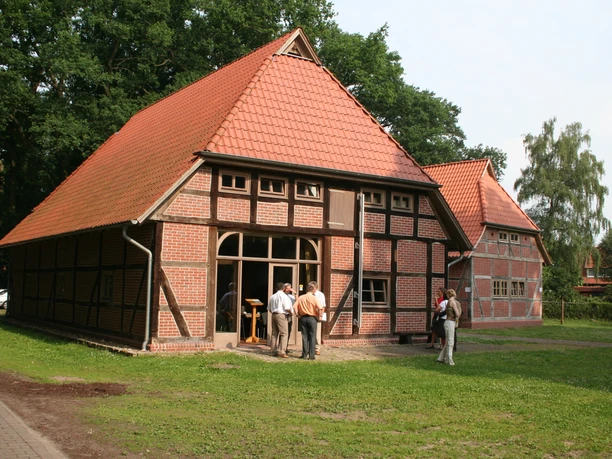 Historic half-timbered barns with red-tiled roofs set in a green, tree-lined setting.