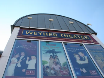 Weyher Theater Eingang des Weyher Theaters mit großen, farbenfrohen Werbepostern der aktuellen Aufführungen.