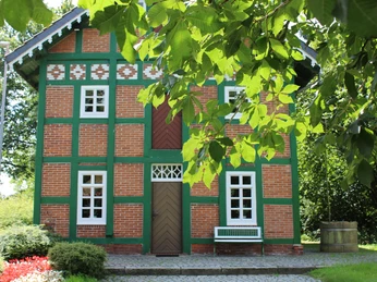 Spieker Lahausen Ein rot geklinkertes Fachwerkhaus mit grünen Holzbalken, umgeben von Bäumen und gepflastertem Weg.