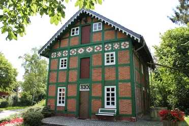 Spieker Lahausen Ein traditionelles Fachwerkhaus mit Ziegelwänden und grünen Akzenten, umgeben von Bäumen und Blumen.