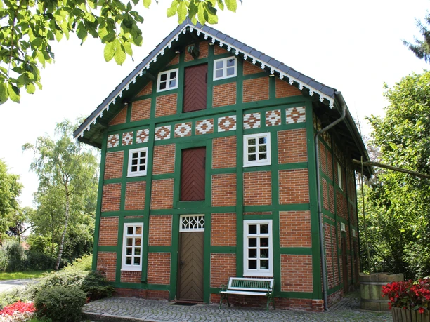 Spieker Lahausen Ein traditionelles Fachwerkhaus mit Ziegelwänden und grünen Akzenten, umgeben von Bäumen und Blumen.