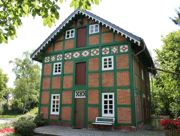 Spieker Lahausen Ein traditionelles Fachwerkhaus mit Ziegelwänden und grünen Akzenten, umgeben von Bäumen und Blumen.