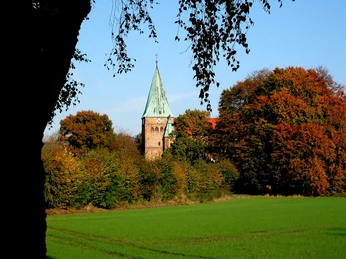Felicianus Kirche Weyhe Felicianus Kirche Weyhe hinter buntem Herbstlaub, Spitzdach mit Turmspitze und Wiesen im Vordergrund.