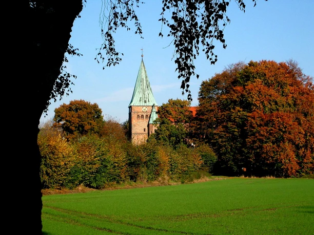 Felicianus Kirche Weyhe Felicianus Kirche Weyhe hinter buntem Herbstlaub, Spitzdach mit Turmspitze und Wiesen im Vordergrund.