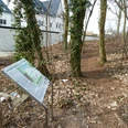 Ein Wanderweg führt durch einen lichten Wald, gesäumt von Schildern, die historische Bedeutung erläutern.