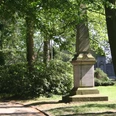 Steinernes Kriegerdenkmal von Bäumen umgeben, gedenkt an Konflikt von 1870/71; grüne Parkumgebung.