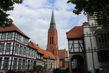 Parish church of St. Martin in Nienburg surrounded by half-timbered buildings, under a cloudy sky.
