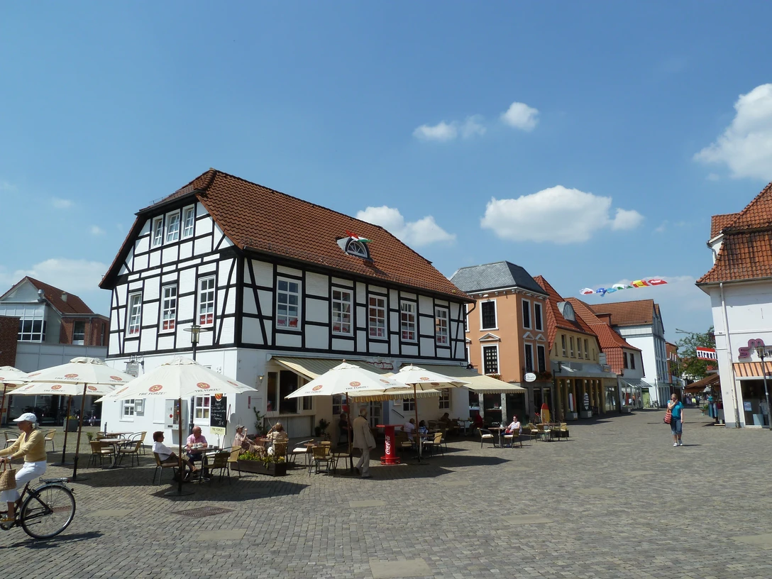 Pforthaus Ein historisches Fachwerkgebäude mit Café-Terrasse und Sonnenschirmen auf einem belebten Platz.