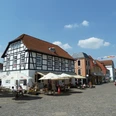 Pforthaus Ein historisches Fachwerkgebäude mit Café-Terrasse und Sonnenschirmen auf einem belebten Platz.