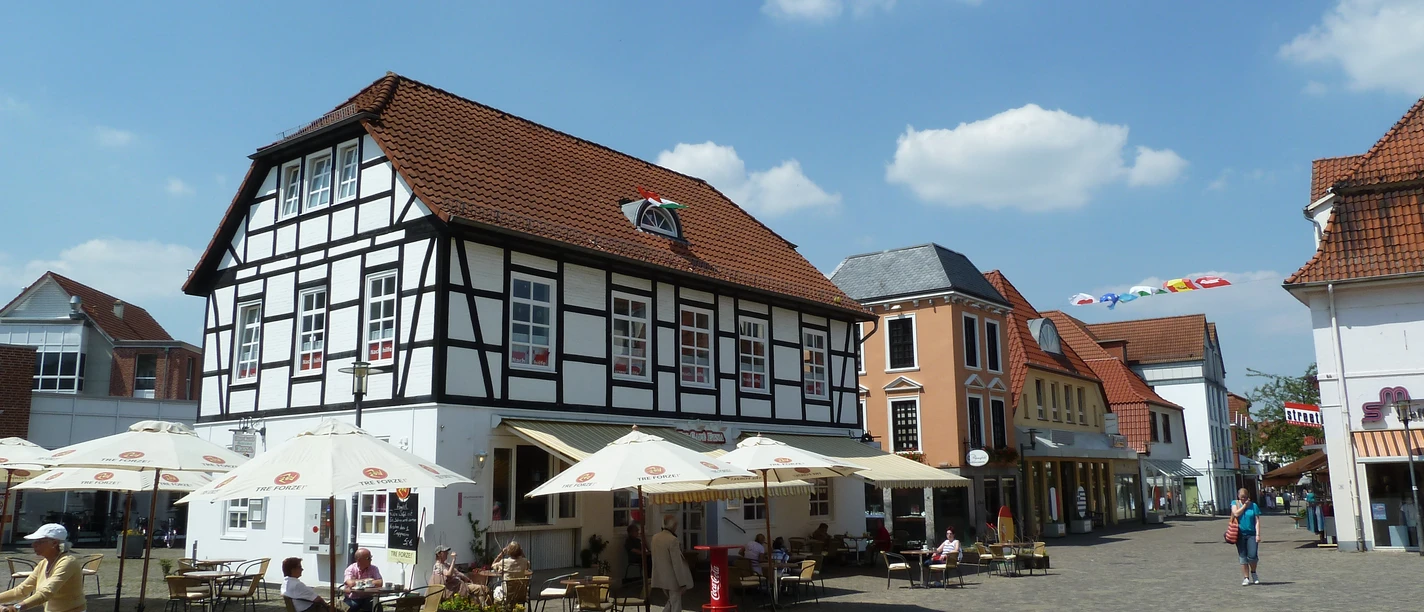 Pforthaus Ein historisches Fachwerkgebäude mit Café-Terrasse und Sonnenschirmen auf einem belebten Platz.