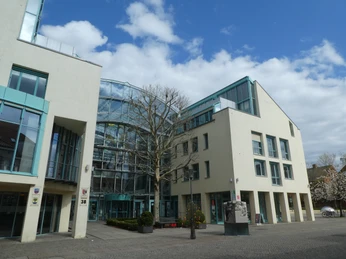 Rathaus Achim Modernes Gebäude mit Glasfronten und hellen Fassaden, umgeben von blühenden Bäumen unter blauem Himmel.