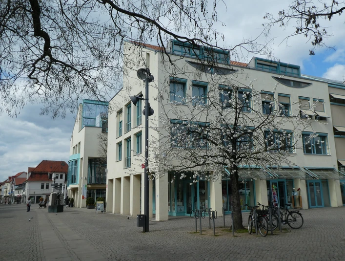 Moderne Architektur des Rathauses Achim mit blühendem Baum im Vordergrund und offener Platzfläche.