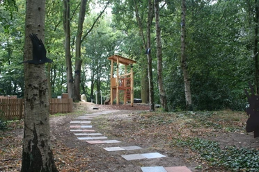 Spielplatz im Rathauspark Achim mit Holzspielgeräten, umgeben von Bäumen und einem gepflasterten Weg.
