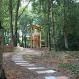 Spielplatz im Rathauspark Achim mit Holzspielgeräten, umgeben von Bäumen und einem gepflasterten Weg.