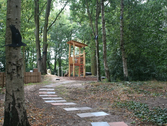 Spielplatz im Rathauspark Achim mit Holzspielgeräten, umgeben von Bäumen und einem gepflasterten Weg.