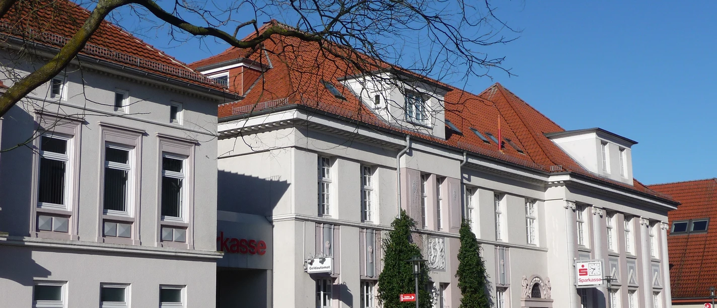 Sparkassengebäude Achim Historisches weißes Gebäude mit rotem Ziegeldach, Sitz der Sparkasse in Achim, Bäume im Vordergrund.