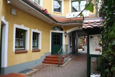 image Gelbes Gebäude mit grünem Eingang und Durchgang, gepflasterter Weg, Laterne und Pflanzen links.