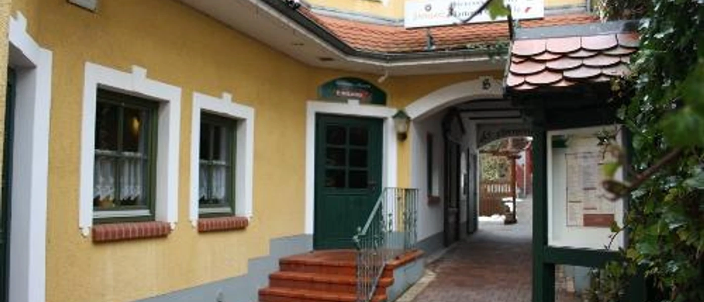 image Gelbes Gebäude mit grünem Eingang und Durchgang, gepflasterter Weg, Laterne und Pflanzen links.