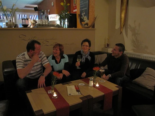 image Vier Personen sitzen lächelnd auf Ledersofas um einen Tisch mit Getränken in einer Bar.