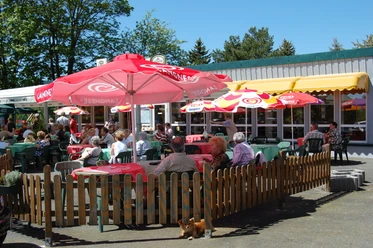 Outdoor terrace of a café with guests under colorful parasols and rustic wooden fencing.