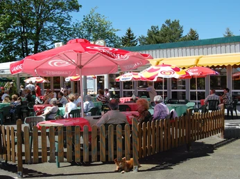 Talsperrenblick Außenterrasse eines Cafés mit Gästen unter bunten Sonnenschirmen und rustikaler Holzabgrenzung.