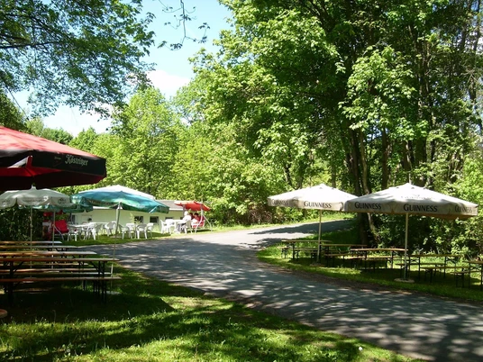 Imbiss Schatzinsel Außenbereich eines Imbisses mit Bänken und Sonnenschirmen im Wald, bietet Schatten und Ruhe.Outdoor area of a snack bar with benches and sunshades in the forest, offers shade and peace.Venkovní prostor s občerstvením, lavičkami a slunečníky v lese nabízí stín a klid.Na zewnątrz znajduje się bar przekąskowy z ławkami i parasolami w lesie, oferujący cień i spokój.Buitengedeelte van een snackbar met banken en parasols in het bos, biedt schaduw en rust.L'area esterna di uno snack bar con panchine e ombrelloni nel bosco, offre ombra e tranquillità.