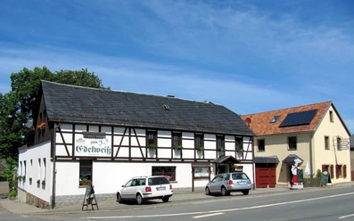 image Ein traditionelles Fachwerkhaus mit Gasthof und zwei geparkten Fahrzeugen davor.