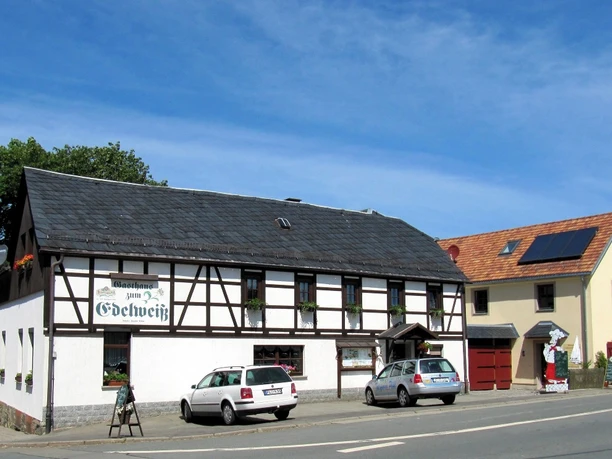 image Ein traditionelles Fachwerkhaus mit Gasthof und zwei geparkten Fahrzeugen davor.