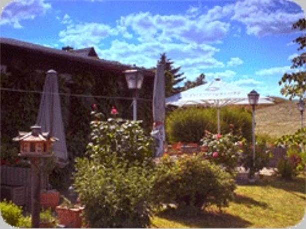 Terasse an der "Schönen Aussicht" Terrasse mit Blumen, Sonnenschirmen und Laternen unter klarem Himmel.