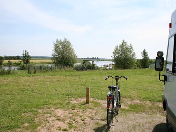 Wohnmobilstellplatz mit Blick auf Flusslandschaft, Fahrradständer im Vordergrund, ruhige Naturumgebung.