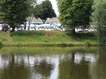 Wohnmobilstellplatz Nienburg Wohnmobilstellplatz am Flussufer mit grünen Bäumen, grasbewachsenen Ufern und geparkten Fahrzeugen.