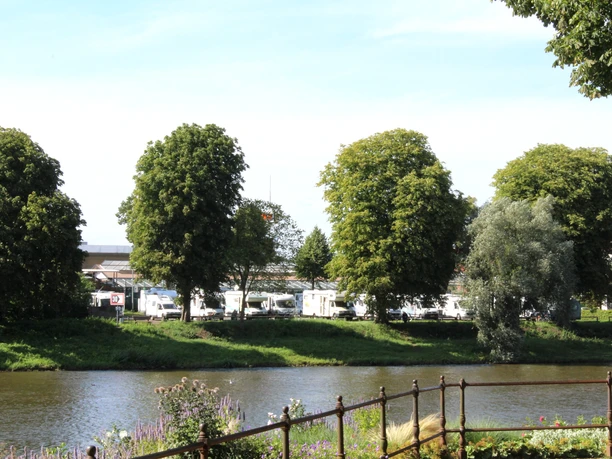 Reisemobilstellplatz Nienburg Reisemobilstellplatz an Flussufer mit Wohnmobilen im Hintergrund und Bäumen im Vordergrund.