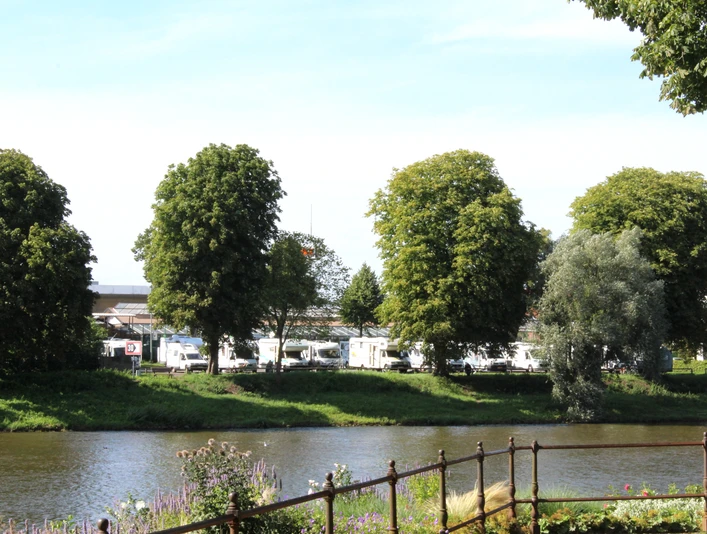 Reisemobilstellplatz Nienburg Reisemobilstellplatz an Flussufer mit Wohnmobilen im Hintergrund und Bäumen im Vordergrund.