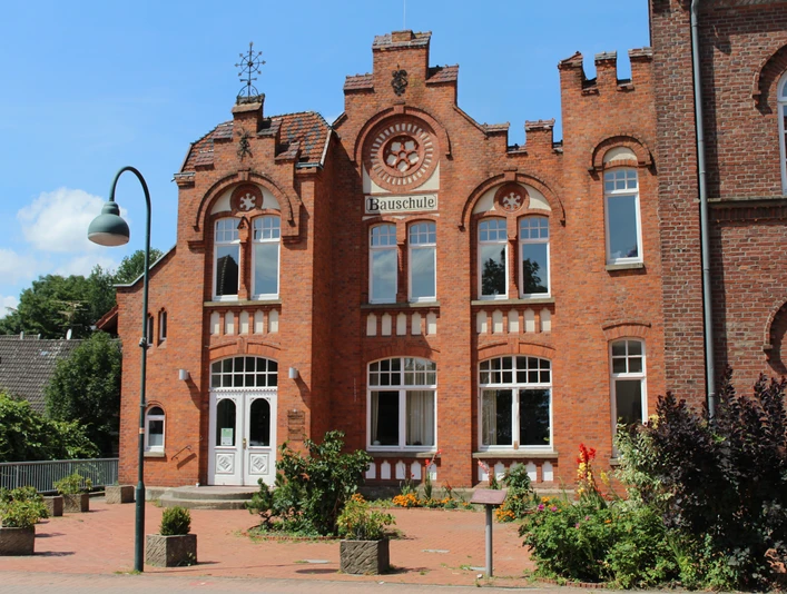 Bauschule Rehburg Backstein-Gebäude der Bauschule Rehburg mit imposanter Fassade und verzierten Fensterbögen bei Sonnenschein.