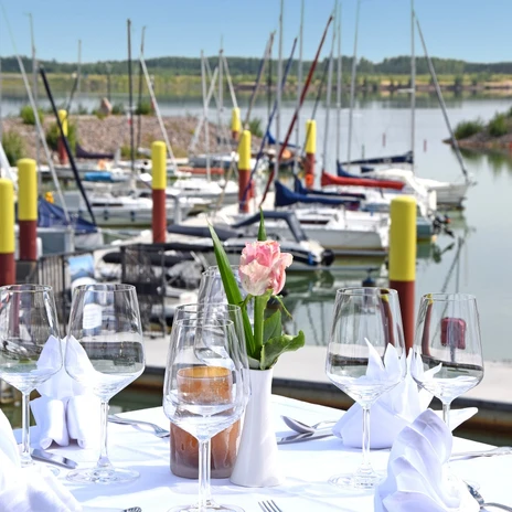 Terrace with set table, view of sailing boats in Zwenkau harbor on a clear day.
