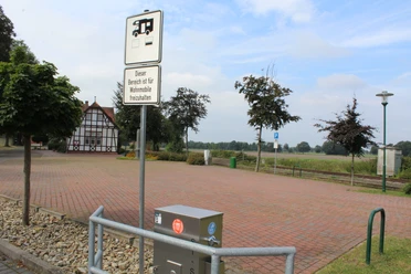 Reisemobilstellplatz Lavelsloh mit gepflasterter Fläche, umrahmt von Bäumen und Fachwerkhaus.
