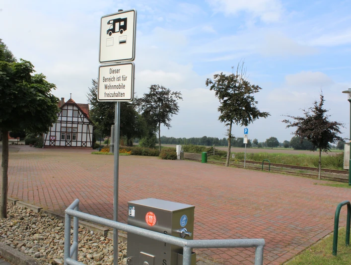Reisemobilstellplatz Lavelsloh mit gepflasterter Fläche, umrahmt von Bäumen und Fachwerkhaus.