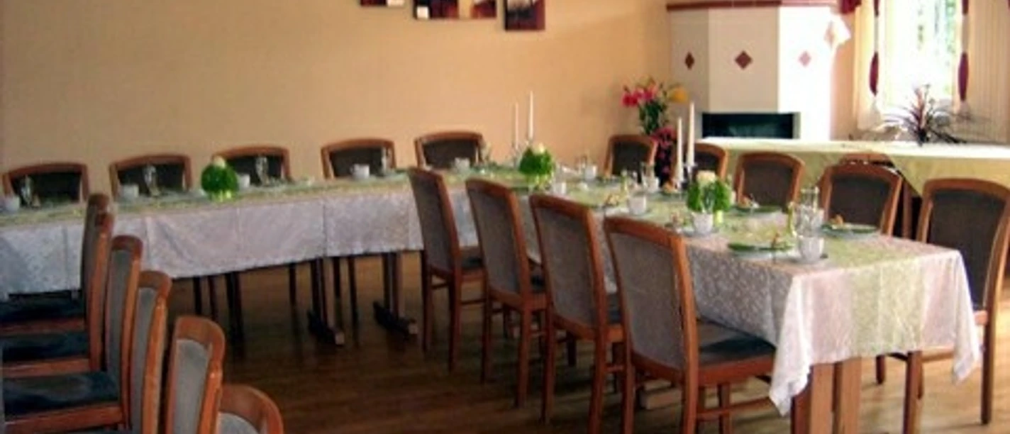 A long table with white tablecloths in a restaurant, decorated with green plants.