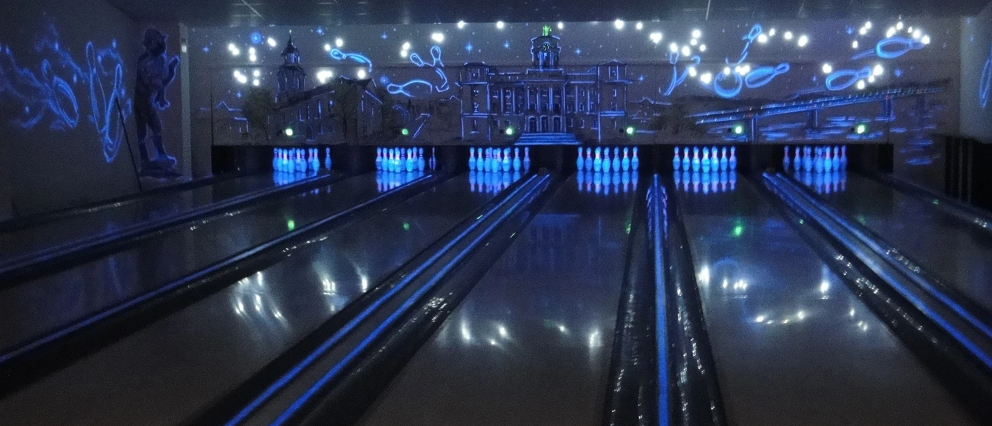 Bowlingbahnen Schwarzlichter auf leuchtenden Bowlingbahnen, mit Stadtbild-Wandgemälde im Hintergrund.