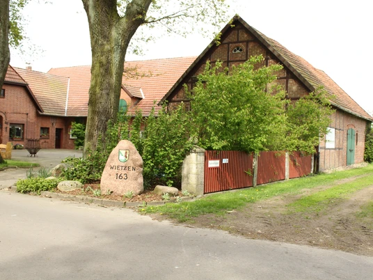 Unser kleiner Hof Wietzen Ein alter Bauernhof mit Backsteingebäuden, umgeben von grünen Bäumen und einem Weg aus Asphalt.