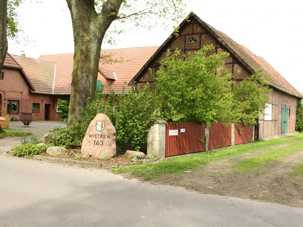 Unser kleiner Hof Wietzen Ein alter Bauernhof mit Backsteingebäuden, umgeben von grünen Bäumen und einem Weg aus Asphalt.