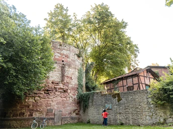 1Diekturm Außenansicht Zwei Personen stehen vor dem Diekturm und schauen sich ein Hinweisschild an der danebenstehenden Mauer an.Two people are standing in front of the tower and looking at a sign on the wall next to it.To personer står foran tårnet og kigger på et skilt på væggen ved siden af.Twee mensen staan voor de toren en kijken naar een bord op de muur ernaast.