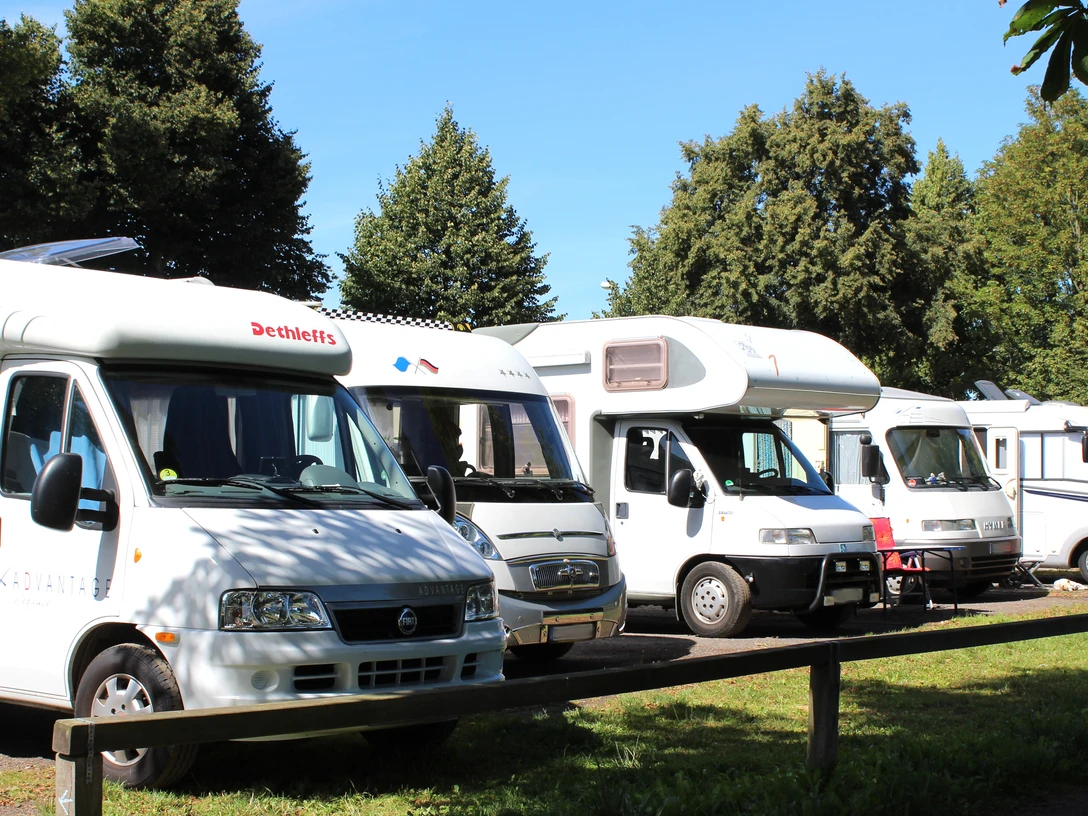 Wohnmobilstellplatz Reihen abgestellter Wohnmobile auf einem Stellplatz, umgeben von Bäumen bei klarem Wetter.