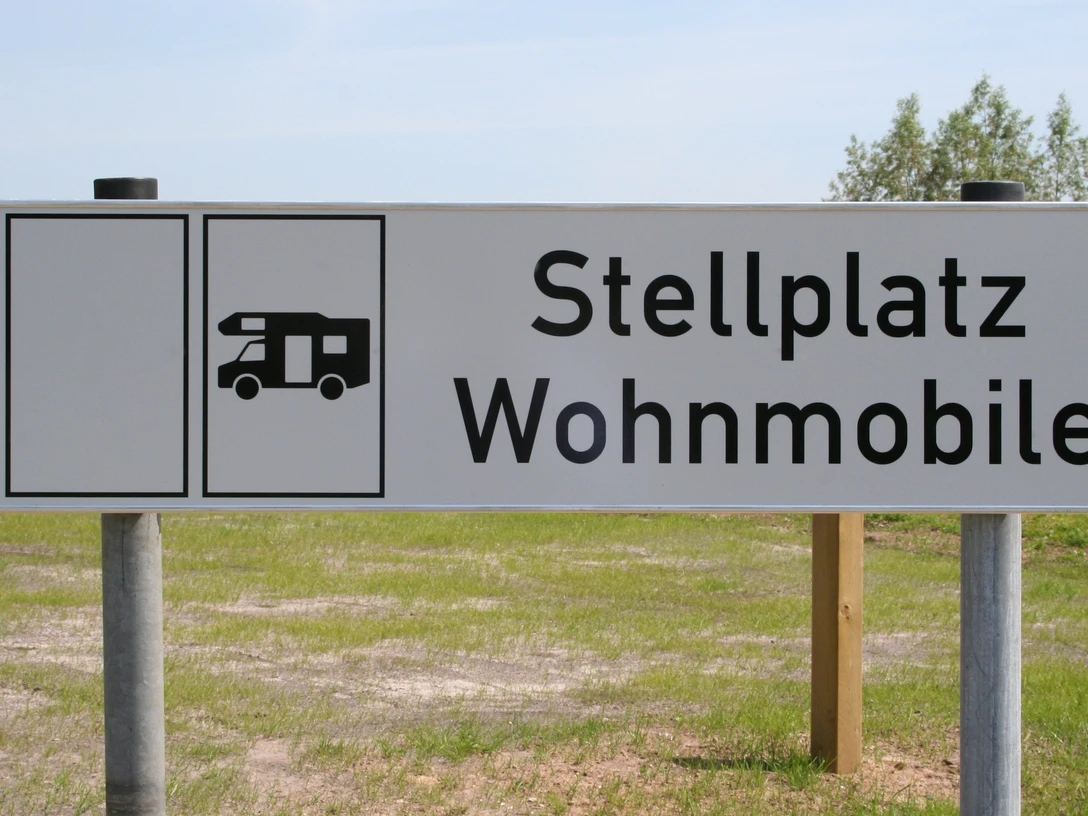 Wohnmobilstellplatz Schild für Wohnmobilstellplatz auf grünem Rasen vor blauem Himmel mit Bäumen im Hintergrund.