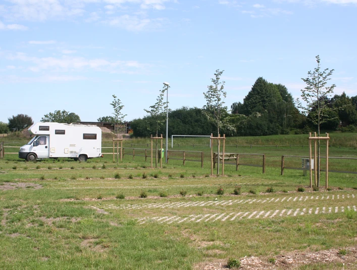 Wohnmobil auf einem Stellplatz mit jungen Bäumen und gepflegter Rasenfläche unter blauem Himmel.