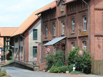 Historische Backsteinmühle mit Brücke und grüner Bepflanzung in einem ländlichen Umfeld.