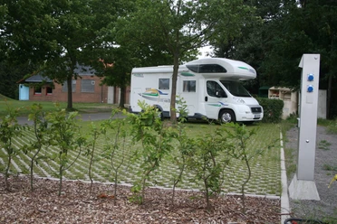 Reisemobilstellplatz Rodewald Ein Reisemobil steht auf einem Stellplatz mit Rasengittern, umgeben von Bäumen und einer Stromsäule.