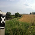 Aerzen - Hansaweg Wanderweg mit Wegweiser am Feldrand, einladender Ausblick auf Wiesen und einen bewölkten Himmel.